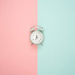 A blue alarm clock on a pink and blue background.