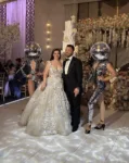 A bride and groom stand posing for a photo while two Disco Ball dancers stand side by side.